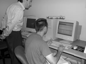 Black and white photo of David looking over student and computer.