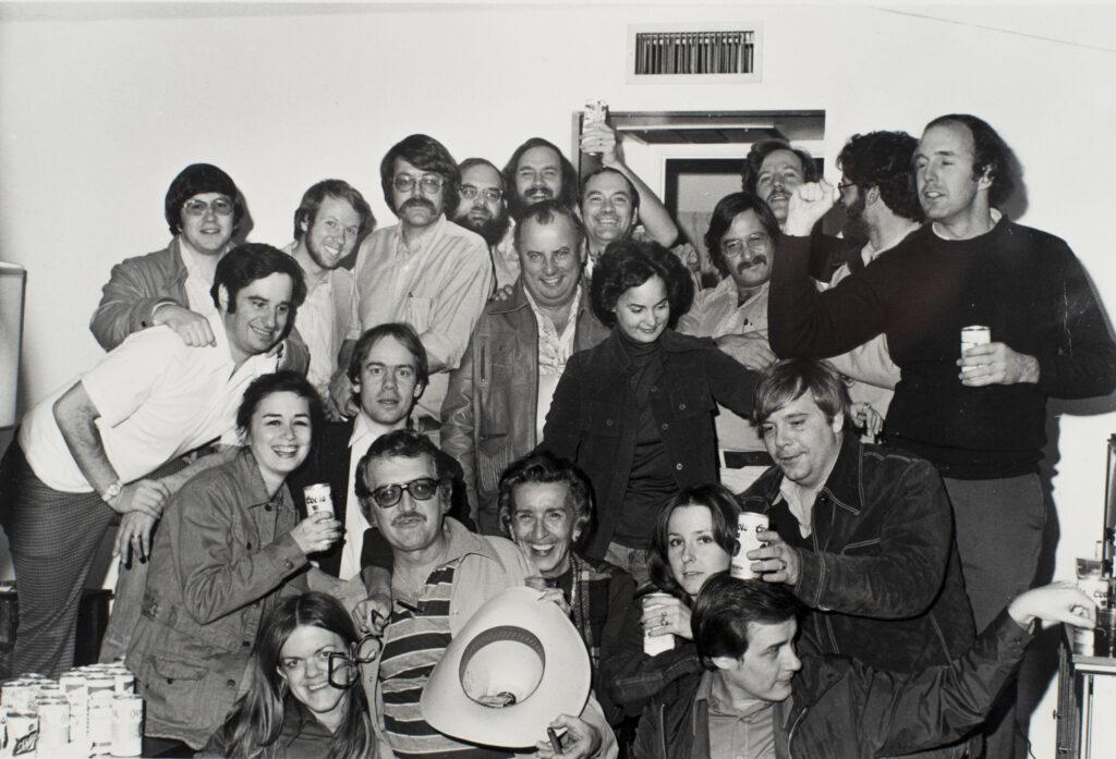 Black and white photo of more than a dozen people posting for a photo. From left, clockwise: George Weisz, Dave Offer, Jack Wimer, Jack McFarren, John Winters, Dave Overton, Tom Renner, John Rawlinson, Diane Hayes, Steve Goldin, Alex Drehsler, Ross Becker, Dan Noyes, Mike Wendland, Dick Cady, Carol Jackson, Kay Nash, Ron Koziol, Susan Irby, Steve Wick, Myrta Pulliam.