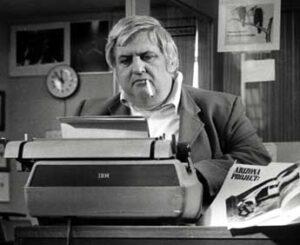 Black and white photo of journalist at typewriter with a cigarette.